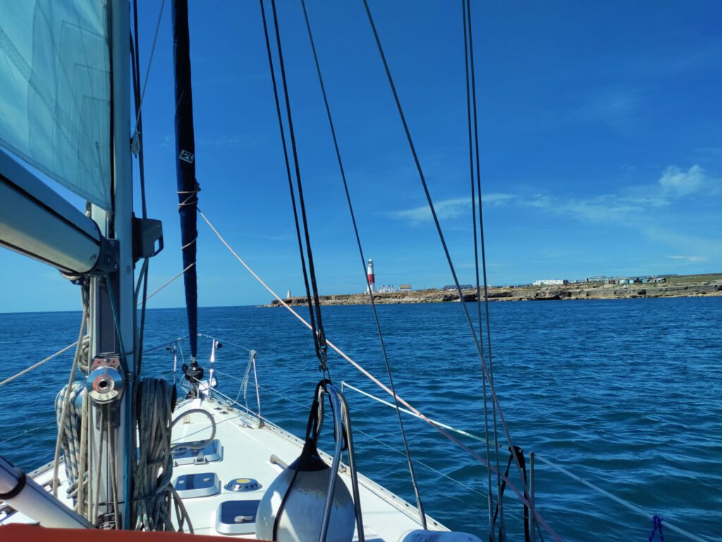 Segelboot steuert auf eine Landspitze mit einem Leuchtturm zu.