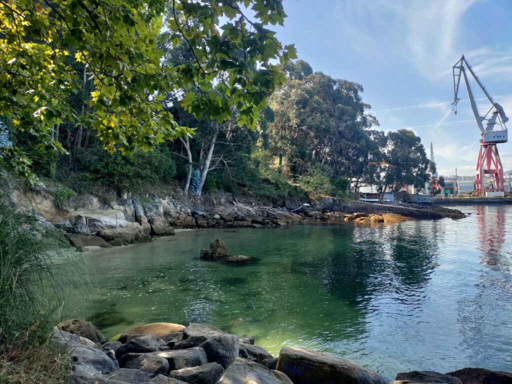 eine schöne Bucht mit klarem Wasser, im Hintergrund steht ein Verladekran.