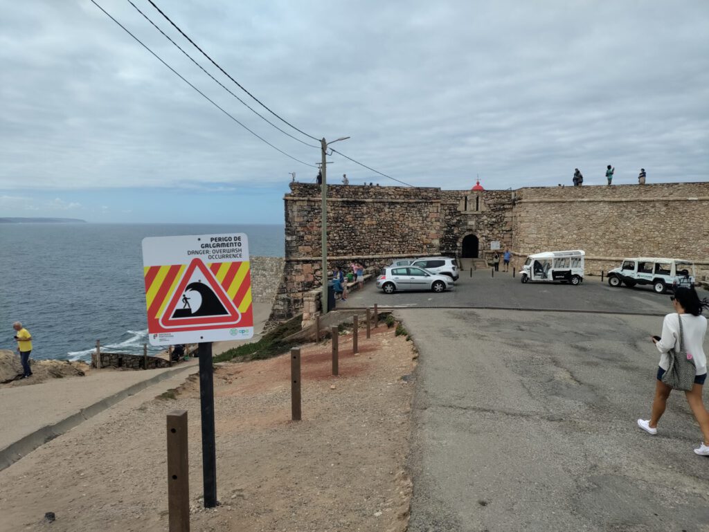 Blick auf das Fort. Im Vordergrund steht ein Schild auf dem ein Mensch von einer riesigen Welle überspült wird.